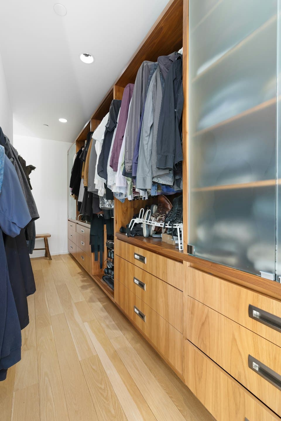 Organized walk-in closet with hanging clothes and wooden cabinetry.