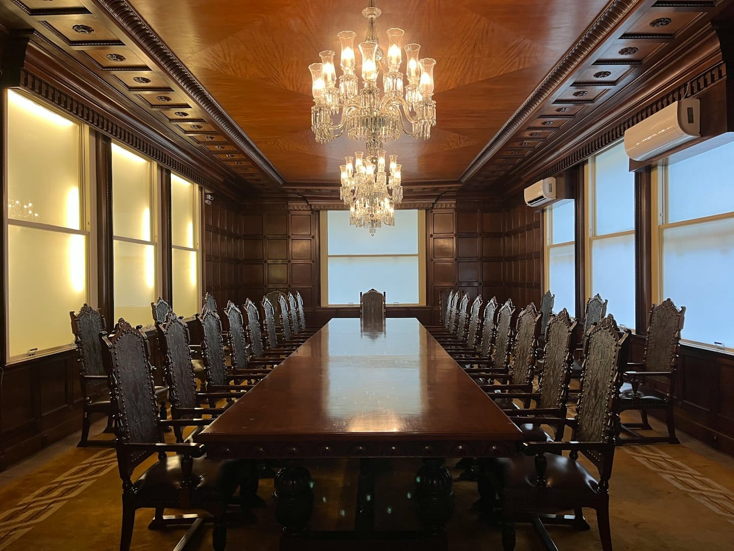 Empty boardroom with polished conference table and ornate chairs.